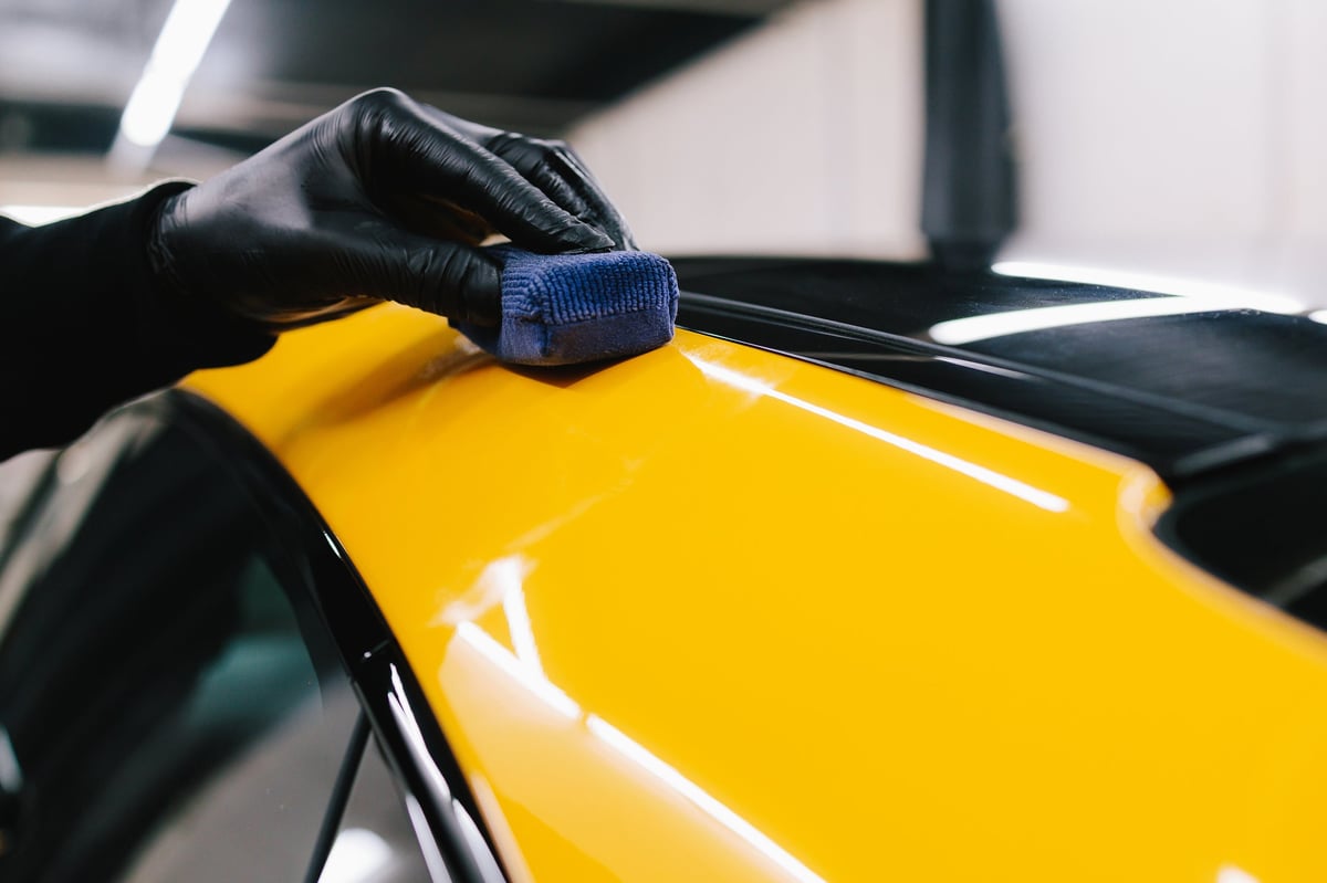 Professional car waxing service with applicator pad on vehicle hood